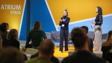 Zwei Frauen halten auf der Bühne der SCCON eine Rede. Davor sitzt Publikum und hört zu.