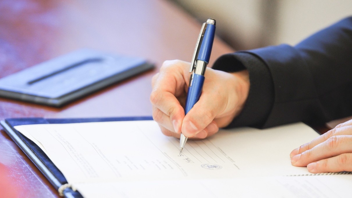 Someone writes with a blue biros on a sheet of paper in a document folder.