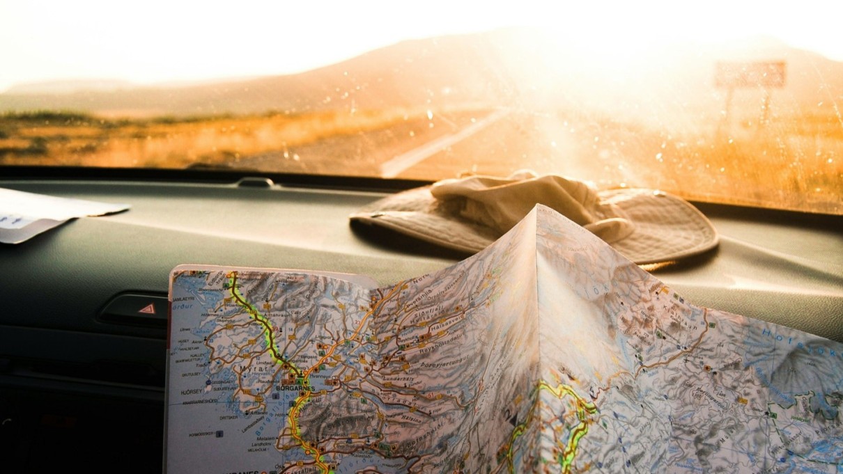 In the background a street in the sun, in the foreground a road map on the dashboard of a car