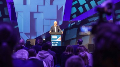 Berlin Mayor Kai Wegner stands at the lectern on the SCCON stage, with the audience in the foreground.