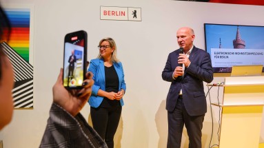 Berliner Bürgermeister Kai Wegner spricht an einem Messestand, neben ihm CDO von Berlin Martina Klement. Ein Handy filmt beide