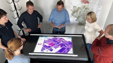 A large screen in the centre, on it the digital twin of Halle an der Saale. Men and women stand around it, the photo is taken fr