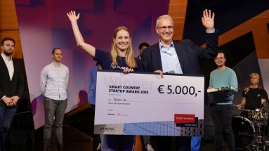 Sieger des Smart Country Startup Awards SUMM AI auf der SCCON Bühne, ein Mann und eine Frau mit einem großen Scheck in der Hand.