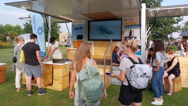 In the background, the Info-Mobil of the Smart Border Region; in the foreground, men and women talking and gathering information